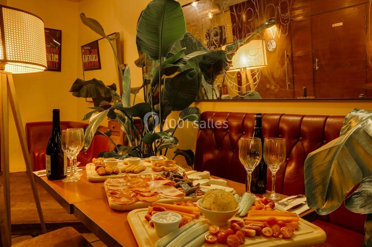 Table dressée dans un restaurant chaleureux avec planches de charcuterie, fromages, légumes et bouteilles de vin rouge.
