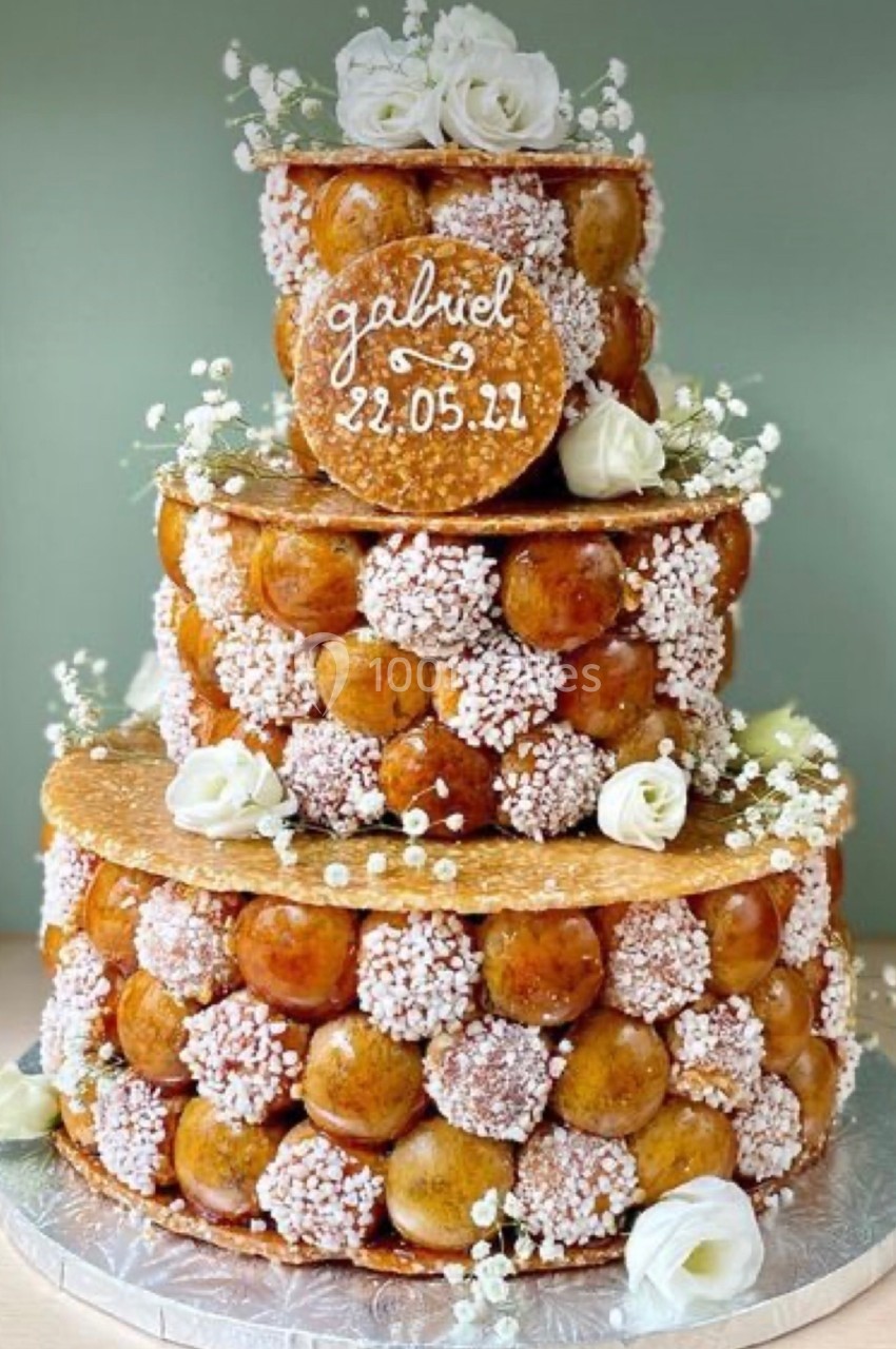 Pièce montée en choux caramélisés décorée de fleurs blanches et d'une inscription manuscrite sur le dessus.