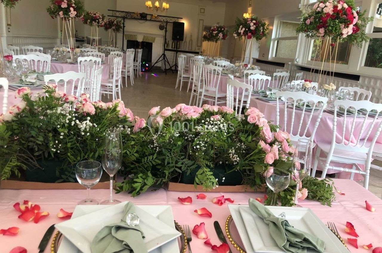Salle de réception décorée avec des fleurs roses, des nappes roses et des chaises blanches, prête pour un événement.