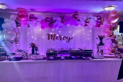Miniature Location salle Triel-sur-Seine (Yvelines) - Malar évenements #23 Buffet décoré avec des ballons roses et blancs, plats variés, et un cochon rôti sur une table drapée de blanc.