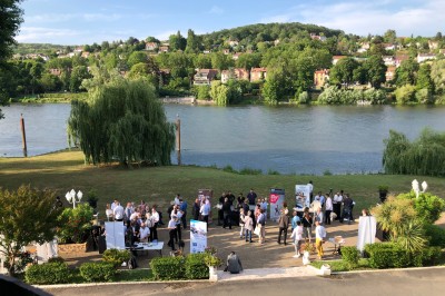 Groupe de personnes rassemblées en extérieur près d'une rivière, entourées de verdure et de stands d'exposition.