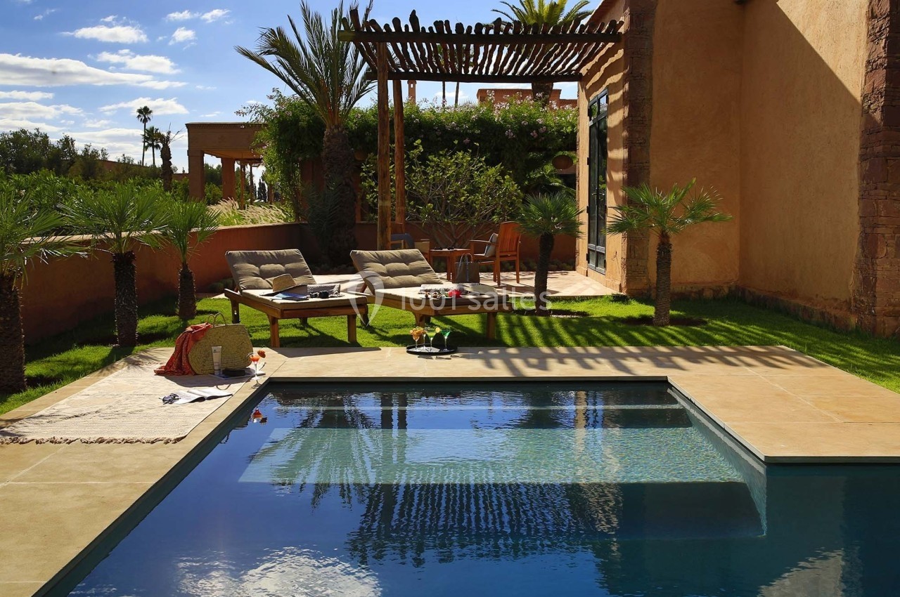 Terrasse avec piscine, transats, table basse et pergola en bois, entourée de palmiers et d'un jardin verdoyant.