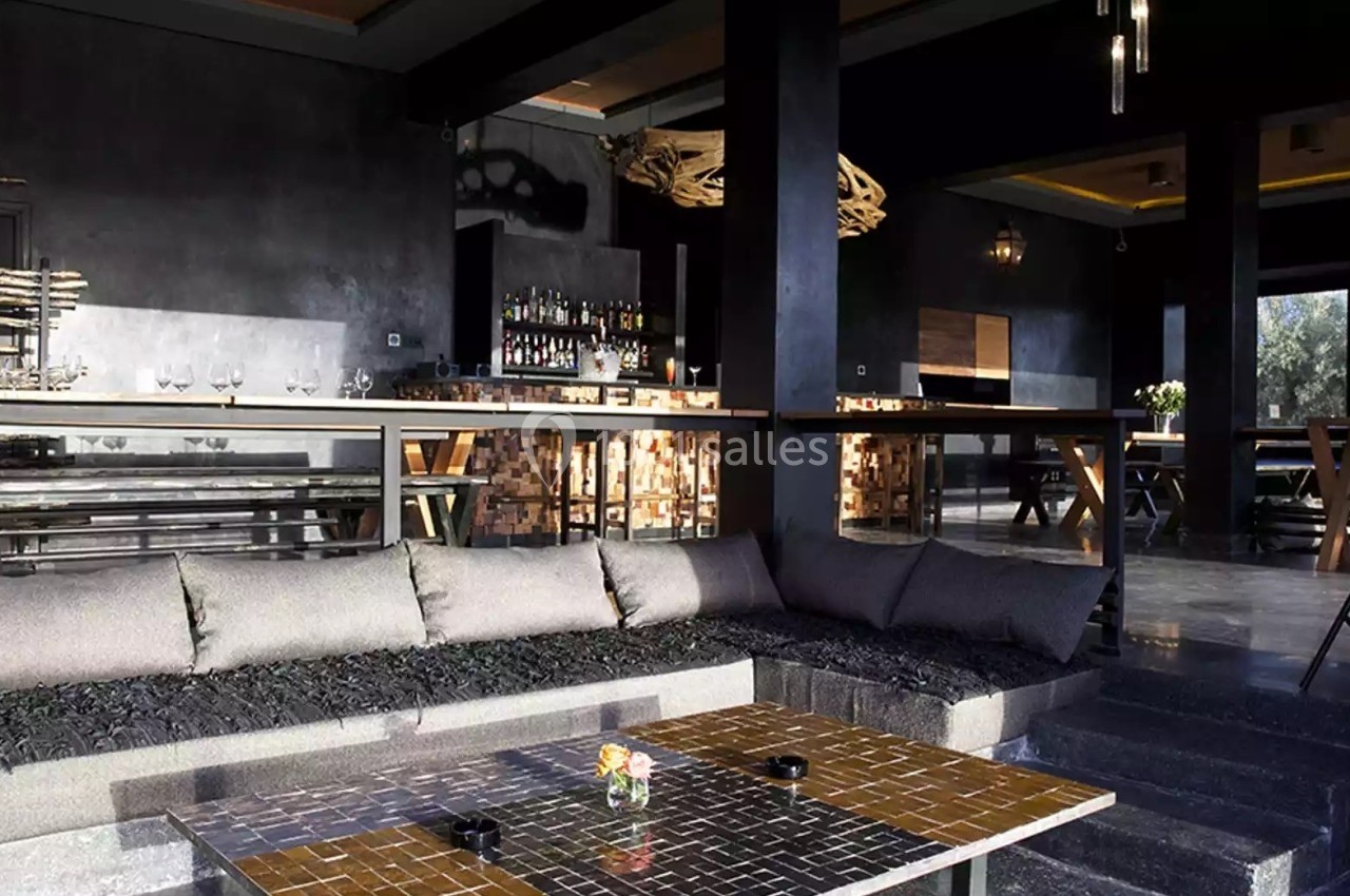 Espace intérieur moderne avec banquettes, table basse en mosaïque, bar en arrière-plan et éclairage tamisé.