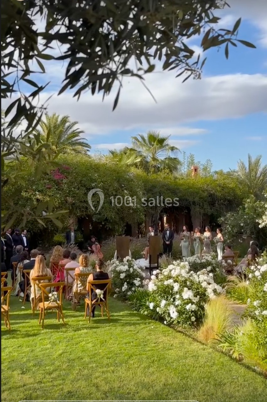 Cérémonie de mariage en extérieur avec invités assis, entourés de fleurs blanches et de végétation luxuriante.