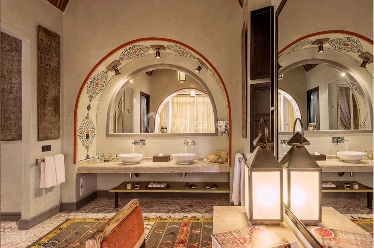 Salle de bain avec deux vasques, miroirs arrondis, tapis colorés et plafond voûté en briques.
