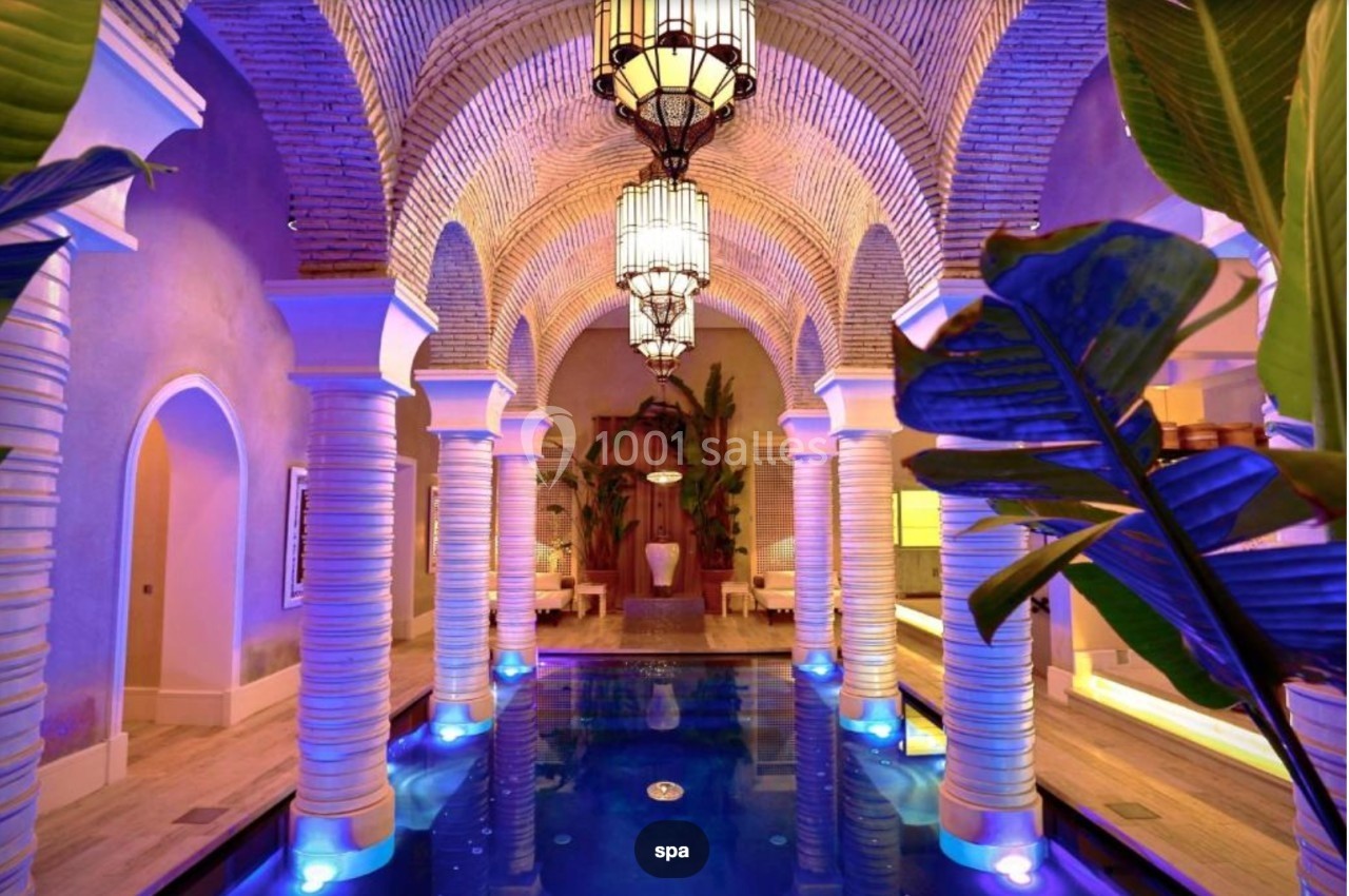Bassin intérieur entouré de colonnes et de plantes, éclairé par des lumières colorées et des lanternes suspendues.