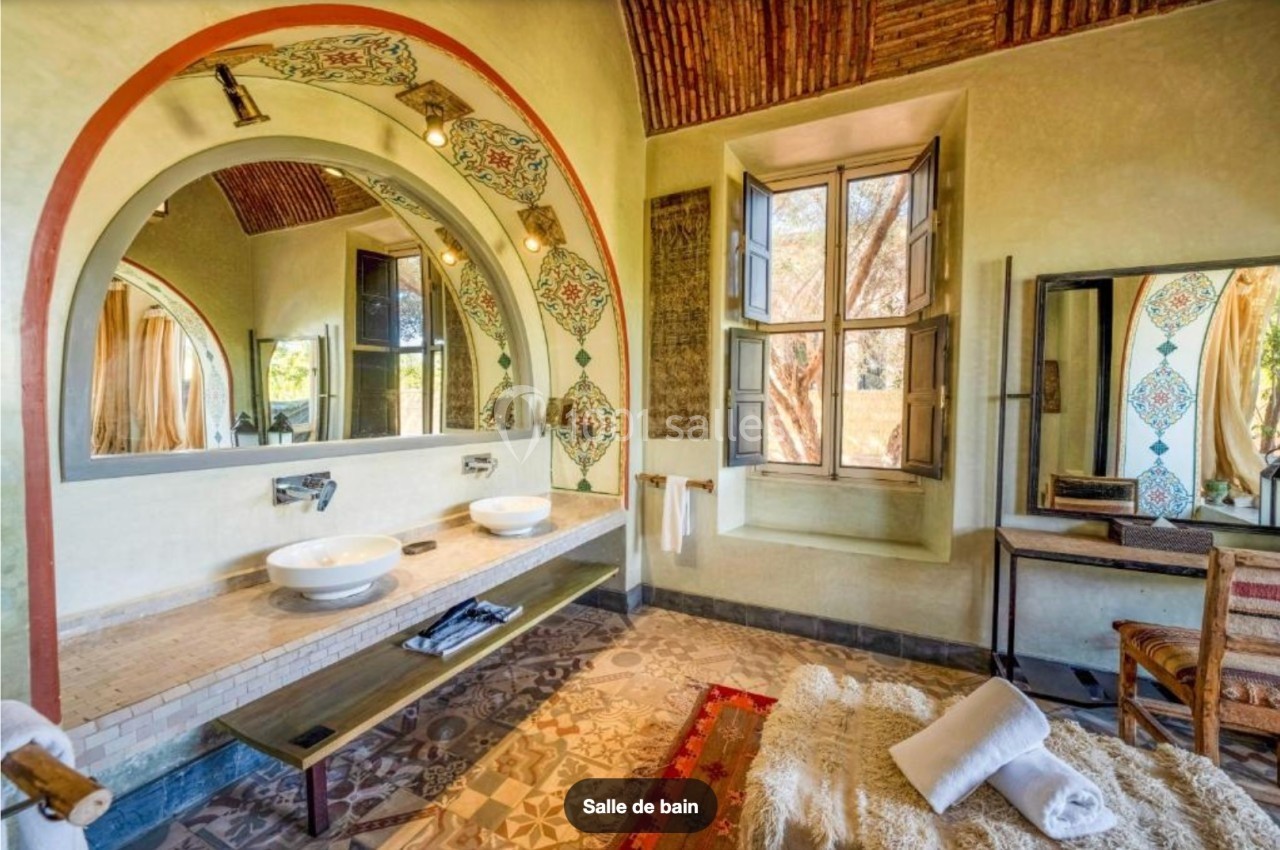 Salle de bain lumineuse avec deux vasques, miroirs ornés, carrelage décoratif et grande fenêtre donnant sur l'extérieur.
