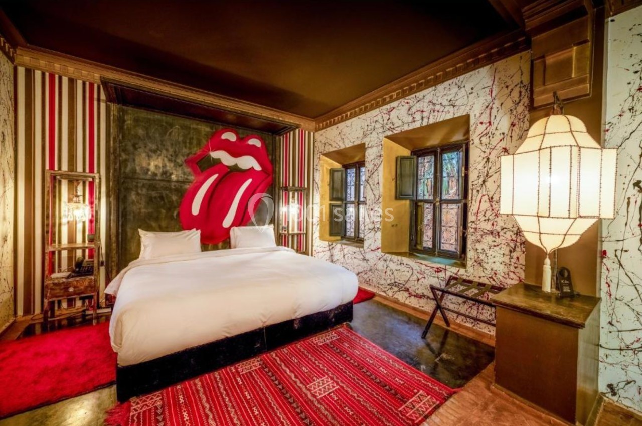 Chambre avec un grand lit, décoration murale artistique, tapis rouge et éclairage chaleureux.