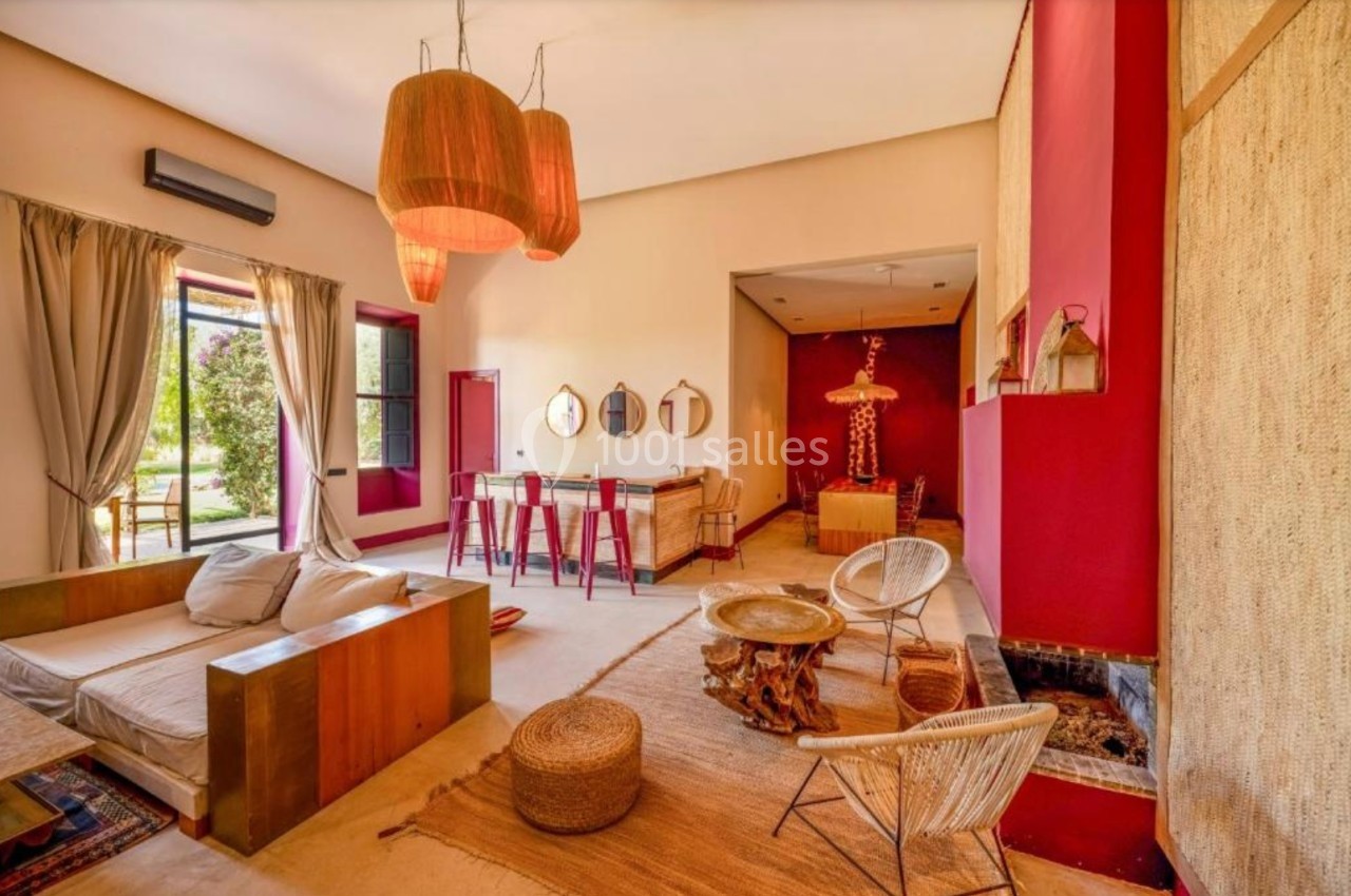 Salon lumineux avec mobilier en bois, tapis en fibres naturelles, murs rouges et grandes fenêtres donnant sur un jardin.