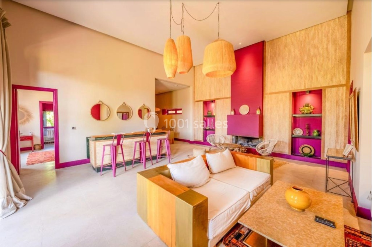Salon lumineux avec murs colorés, mobilier moderne, suspensions en osier et espace salle à manger avec tabourets hauts.