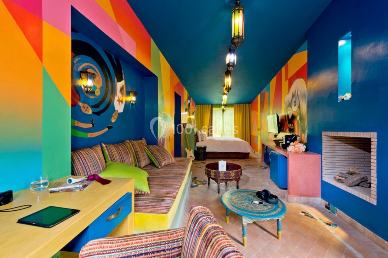 Chambre colorée avec décorations murales vives, canapé, lit, cheminée et éclairage suspendu.