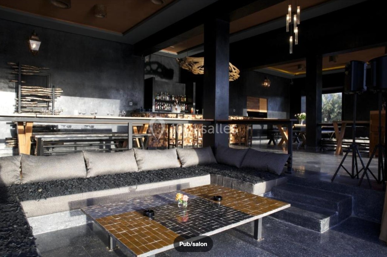 Espace intérieur moderne avec canapé d'angle, table basse et bar en arrière-plan dans une ambiance tamisée.