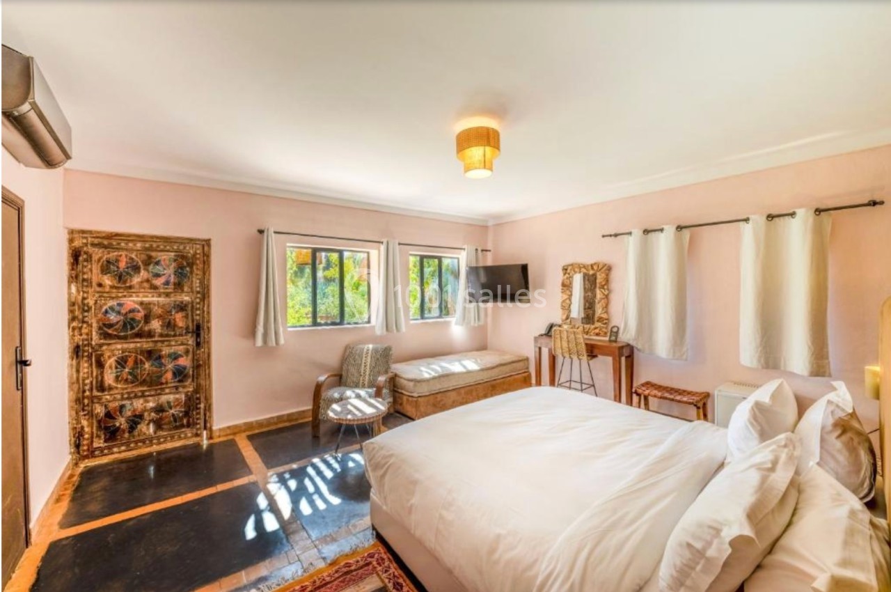Chambre lumineuse avec lit double, décor rustique, fenêtres donnant sur un jardin, et mobilier en bois artisanal.