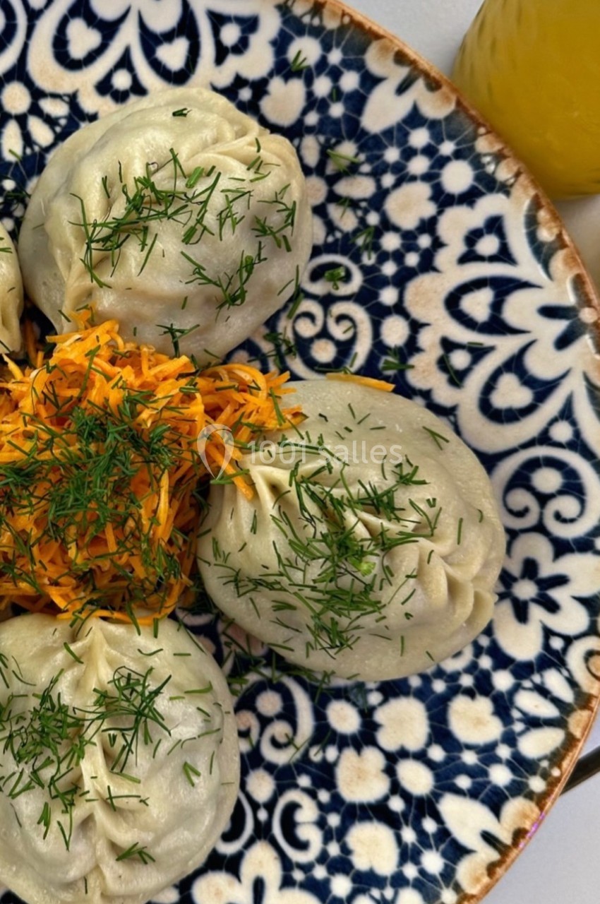Assiette de raviolis garnis d'aneth accompagnés de carottes râpées, présentée sur un plat à motifs bleus.