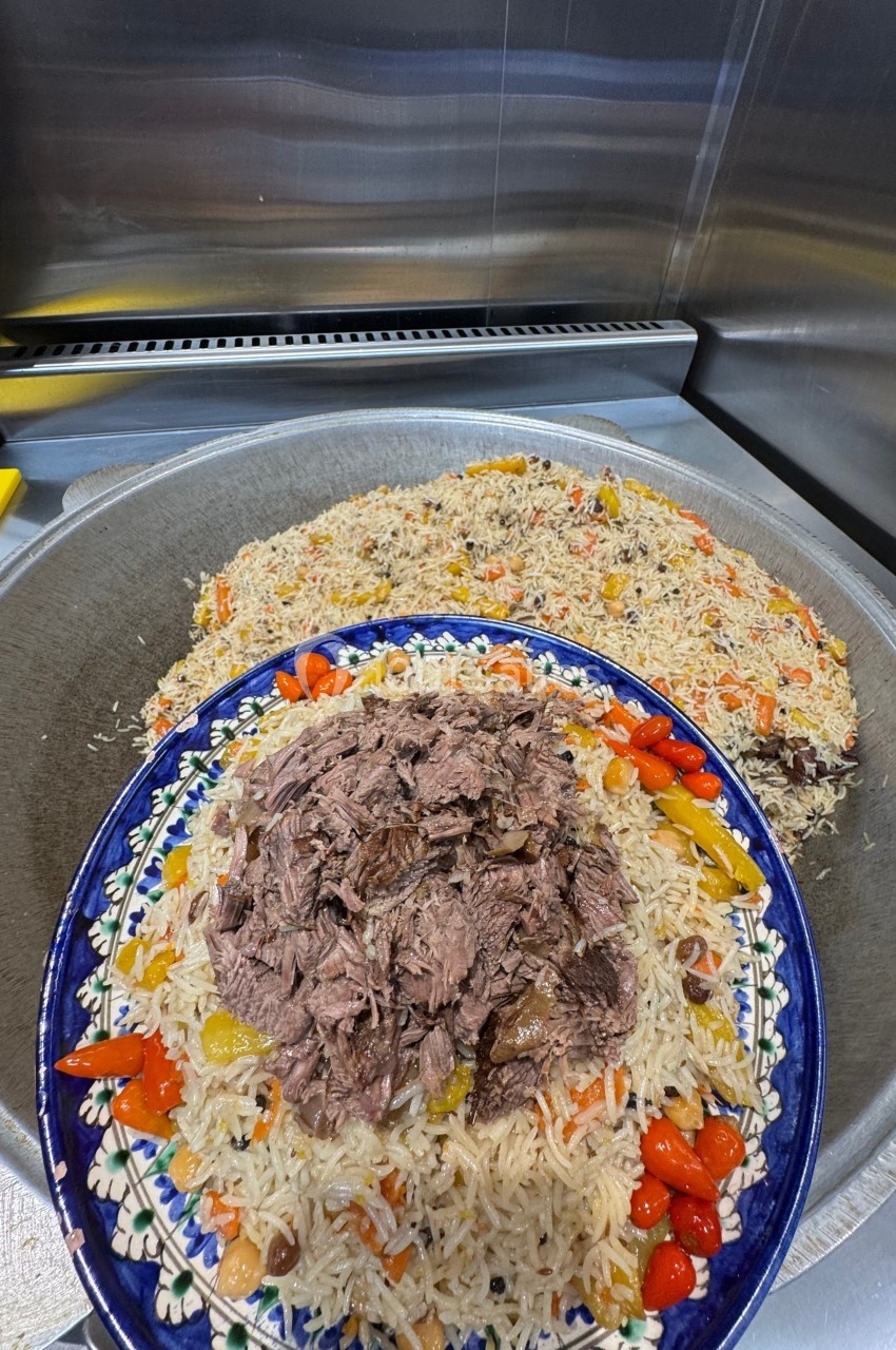 Plat de riz garni de légumes colorés et de morceaux de viande, présenté dans un grand plat décoré.