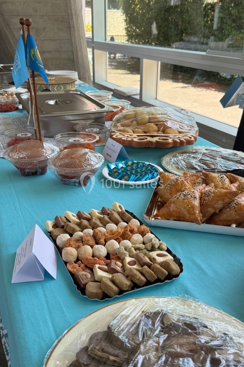 Table garnie de pâtisseries variées, plats salés et desserts disposés sur une nappe bleue dans un cadre lumineux.