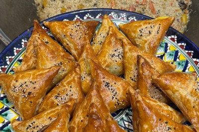 Un homme cuisine de grandes pièces de viande dans une marmite fumante en extérieur, portant un tablier et des gants.