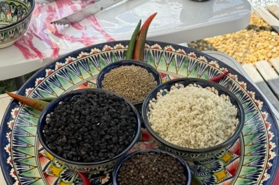 Un homme cuisine de grandes pièces de viande dans une marmite fumante en extérieur, portant un tablier et des gants.