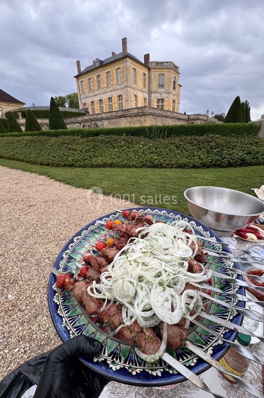 Assiette de brochettes garnies d'oignons et de légumes devant un château entouré de jardins.