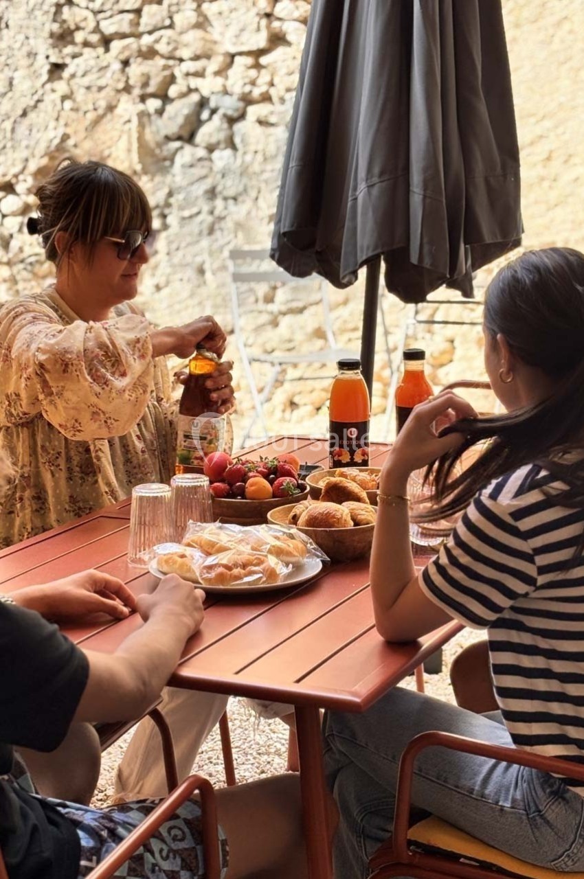 Trois personnes partagent un repas en plein air autour d'une table avec boissons, viennoiseries et fruits.