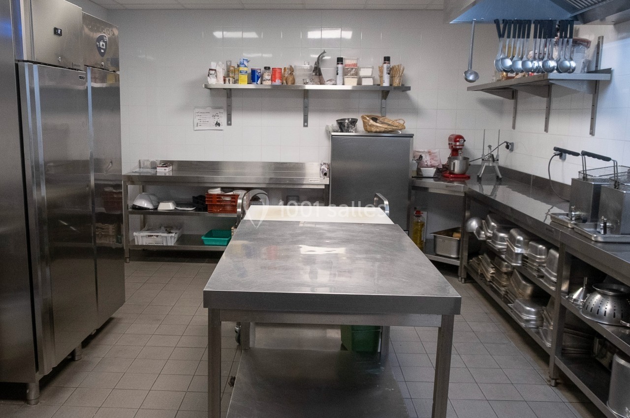 Cuisine professionnelle équipée avec plan de travail en inox, étagères de rangement et appareils électroménagers.
