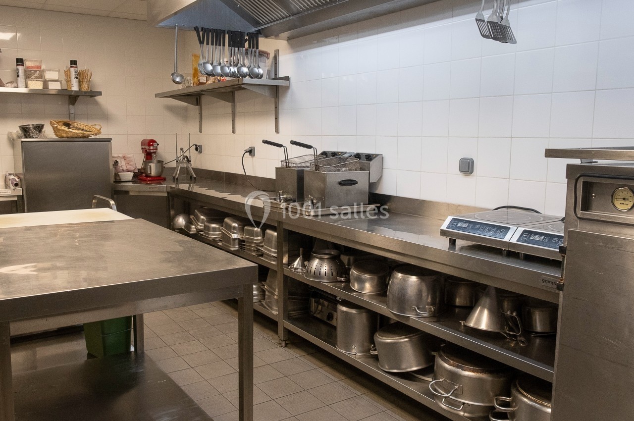 Cuisine professionnelle avec plans de travail en inox, étagères remplies d'ustensiles et équipements de cuisson.