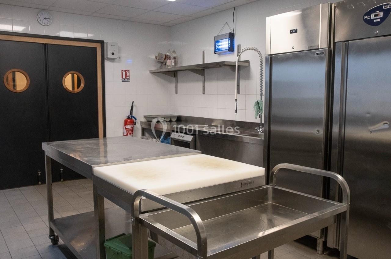 Cuisine professionnelle avec plan de travail en inox, réfrigérateurs, évier et équipement de rangement.