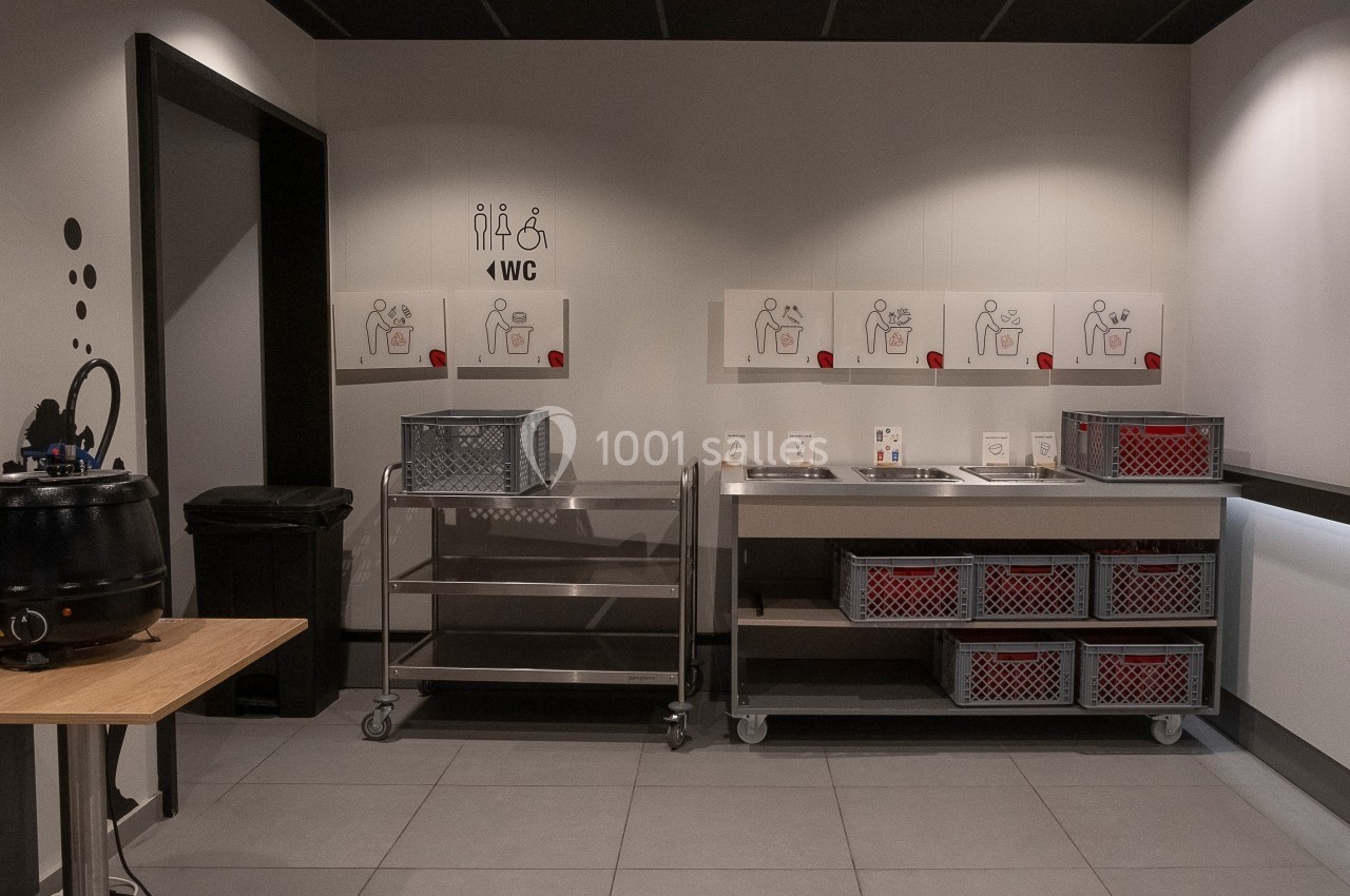 Espace de tri des déchets avec bacs de recyclage et affiches explicatives sur un mur dans un environnement intérieur.