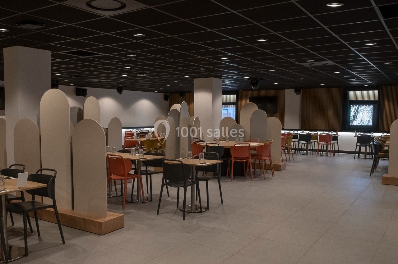 Salle de restaurant moderne avec des tables espacées, des chaises colorées et des séparateurs en forme d'arche.