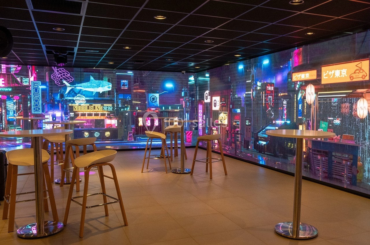 Salle moderne avec tables hautes et décorations murales lumineuses évoquant une ambiance urbaine nocturne futuriste.