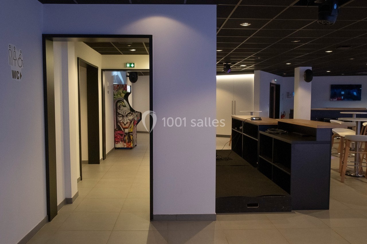 Espace intérieur moderne avec un sol carrelé, un comptoir, des tables hautes et une signalisation pour les toilettes.