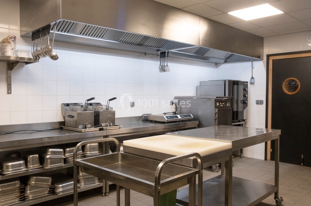 Cuisine professionnelle équipée avec plan de travail en acier inoxydable, friteuse, étagères et hotte d'extraction.