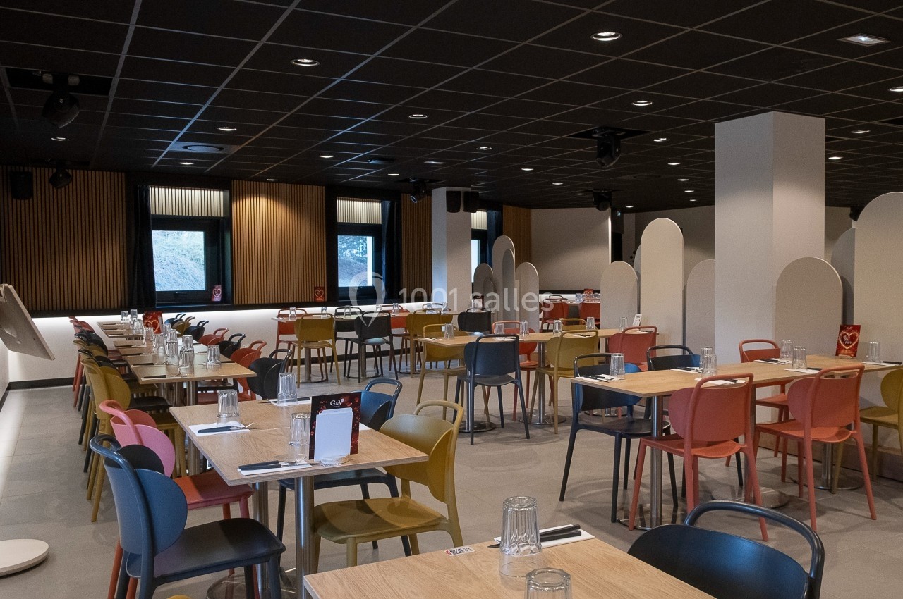Salle de restaurant moderne avec des tables en bois, chaises colorées et cloisons blanches pour séparer les espaces.