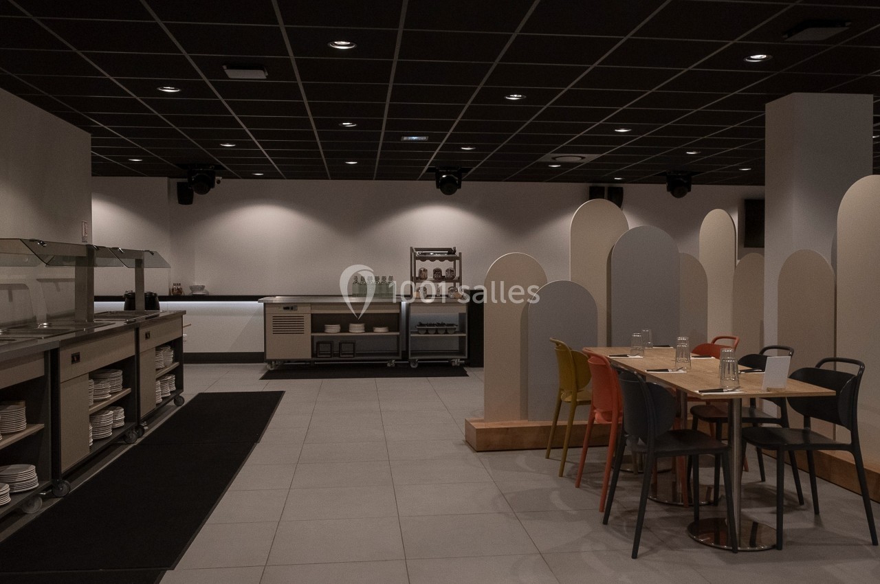 Salle de restaurant moderne avec tables, chaises colorées, buffet en libre-service et cloisons de séparation.