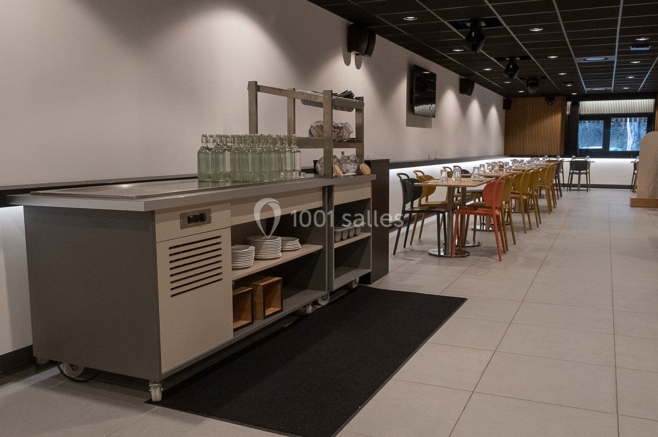 Salle de restaurant moderne avec tables alignées, chaises colorées et un buffet de service en premier plan.