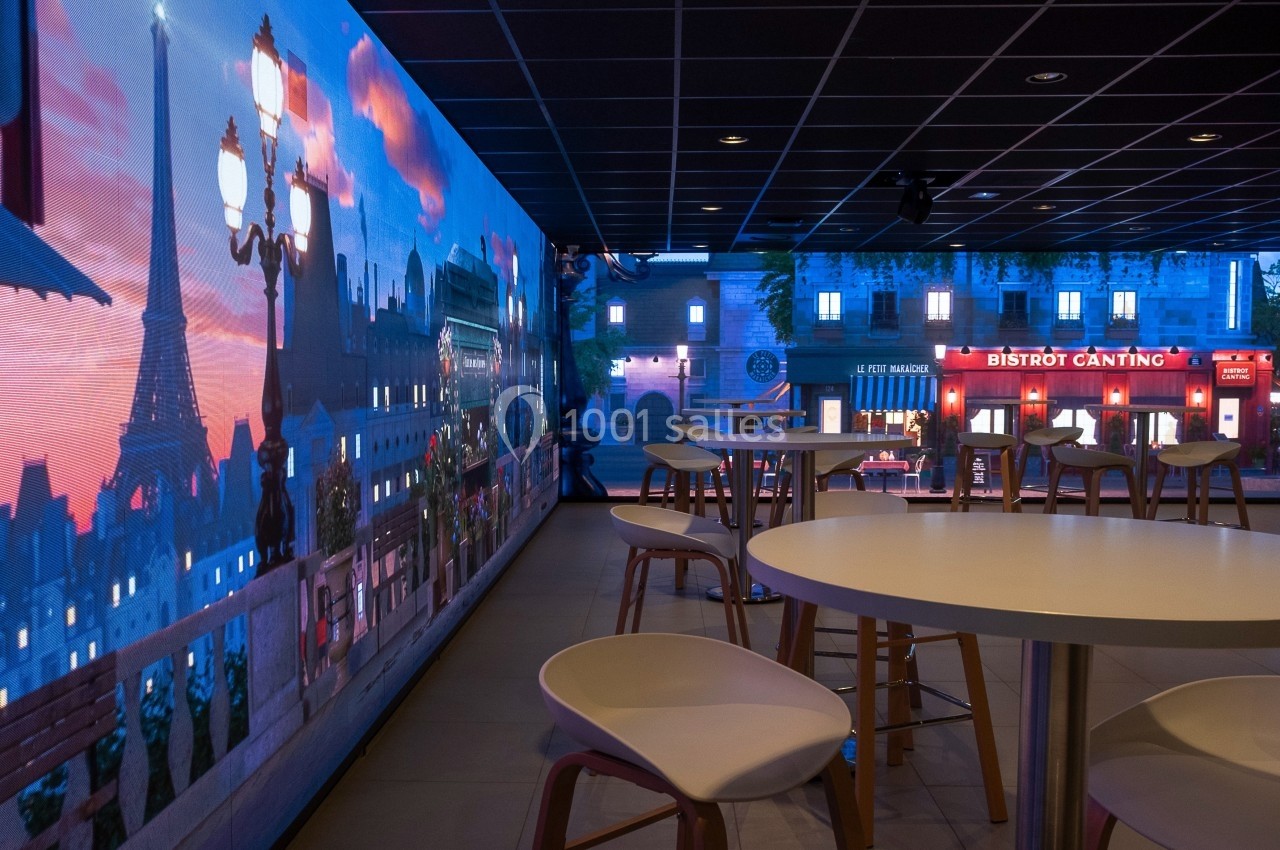 Salle avec tables et chaises, décorée de panneaux lumineux représentant une vue nocturne de Paris.