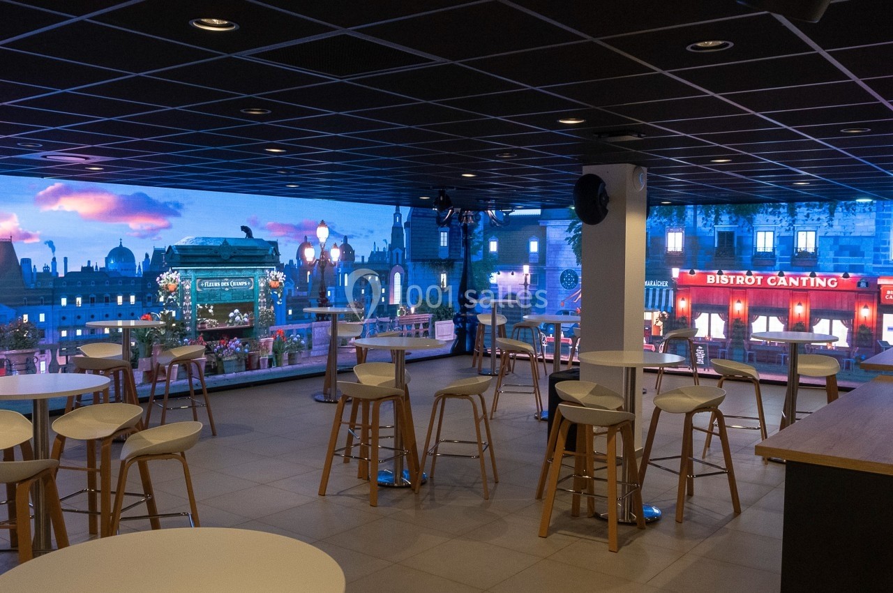 Salle avec tables et tabourets, décor mural représentant une vue de Paris avec bâtiments et enseignes lumineuses.