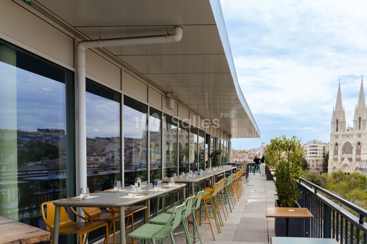 Terrasse panoramique couverte avec tables et chaises jaunes et vertes, vue sur la cathédrale de Marseille.