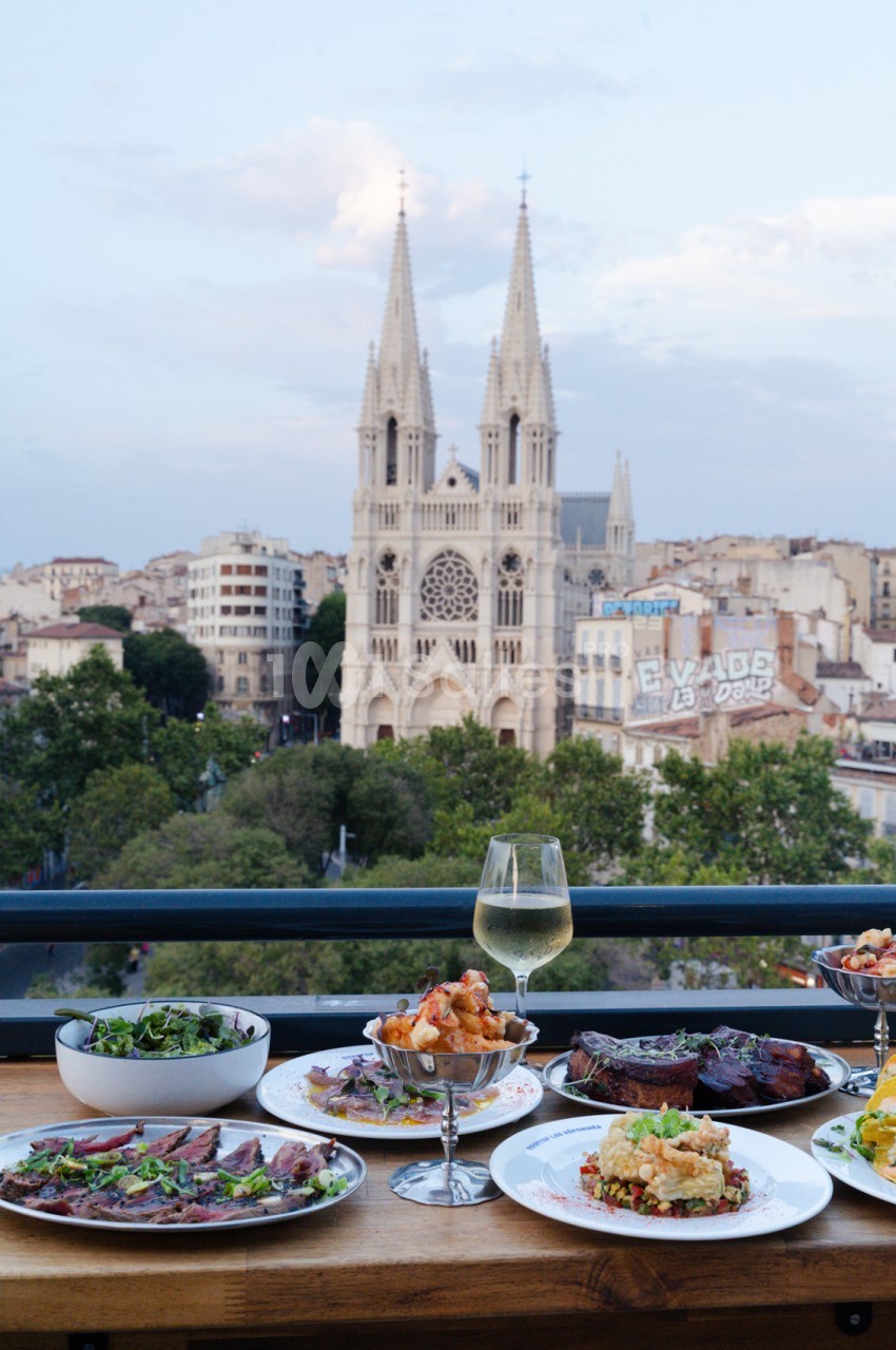 Table dressée avec assiettes, verres et plats - vue depuis une terrasse surplombant la basilique Notre-Dame-de-la-Garde.