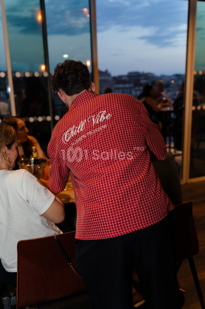 Rooftop en soirée avec convives attablés face à la baie vitrée et vue panoramique sur la ville.