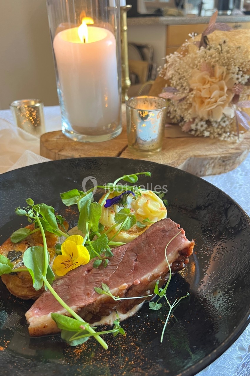 Assiette de viande grillée avec purée, légumes verts et fleurs comestibles, sur une table décorée avec bougie et fleurs…