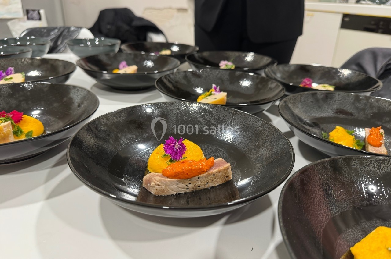 Assiettes noires contenant des plats raffinés avec poisson, purée orange et fleurs comestibles, disposées sur une table.