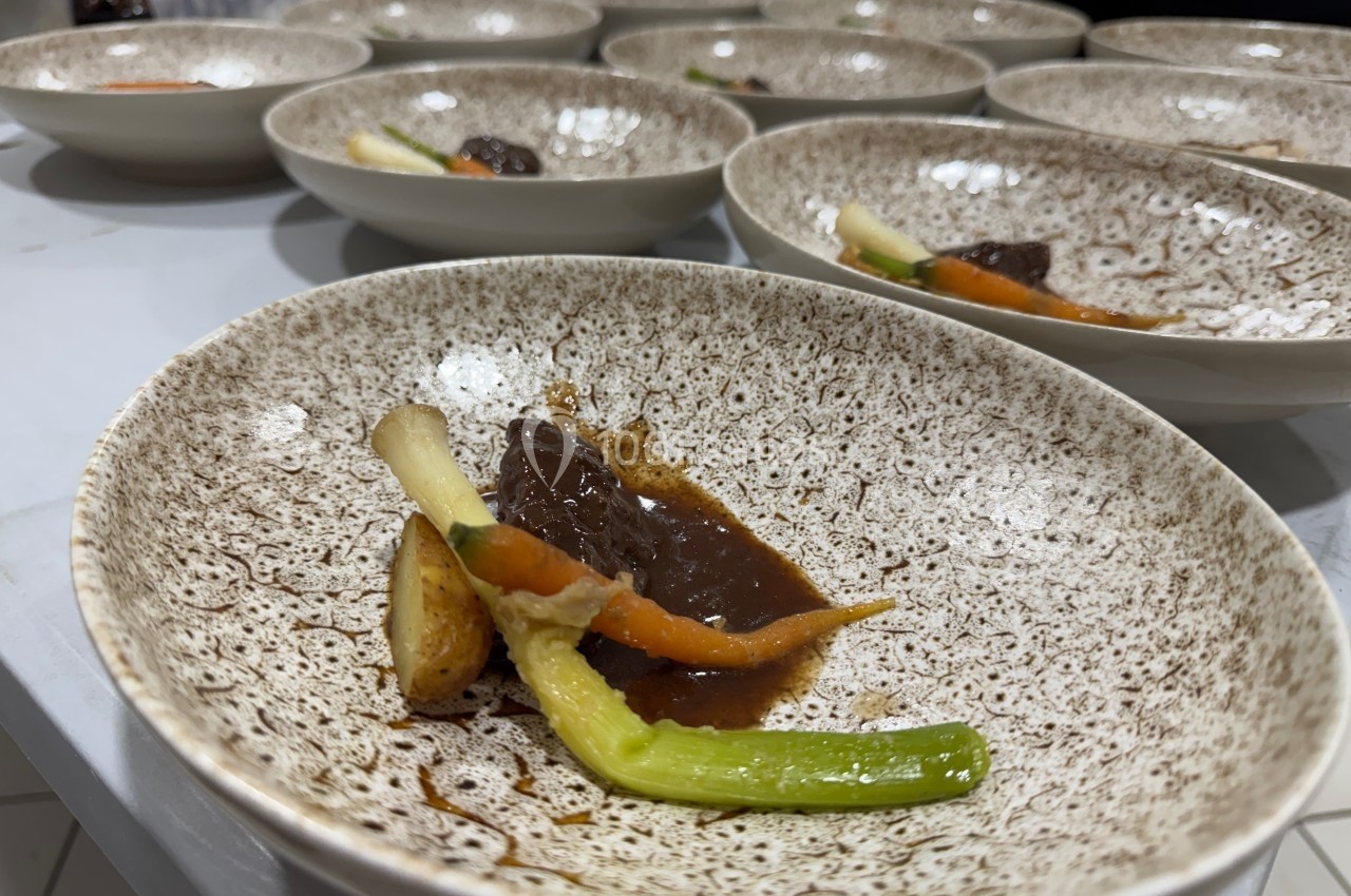 Assiette contenant un plat dressé avec sauce brune, carottes, poireau et pomme de terre sur une table.