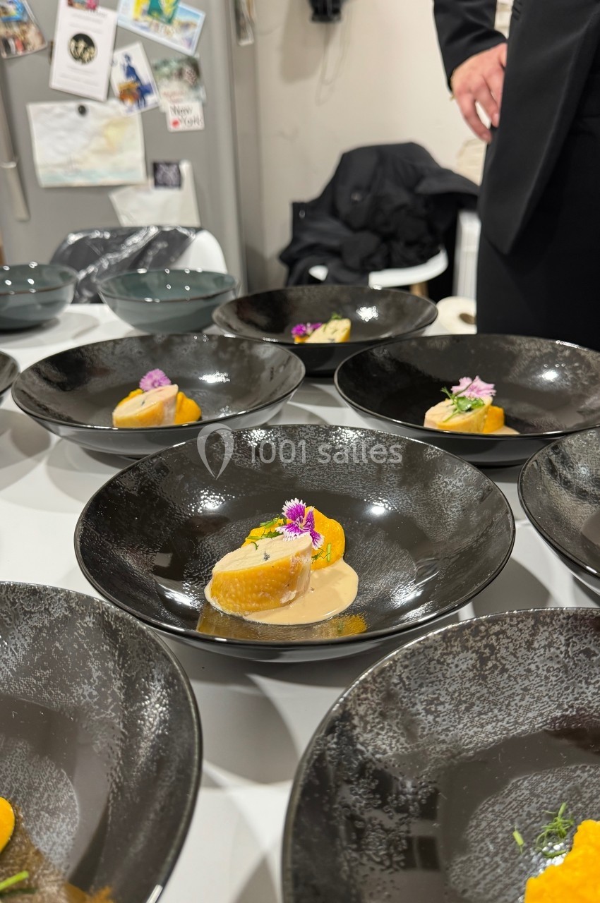 Assiette noire contenant une présentation soignée de mets avec sauce, fleurs comestibles et décorations raffinées.