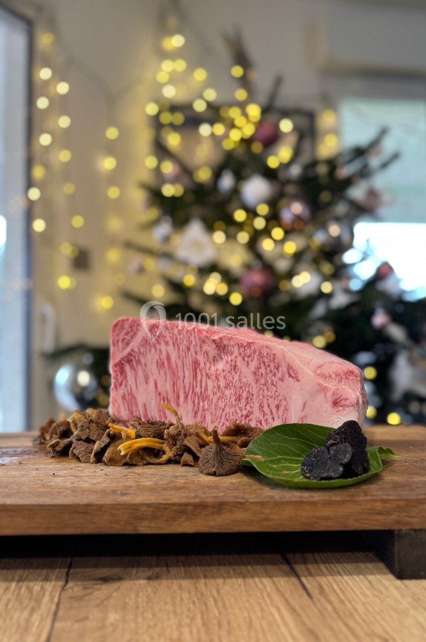 Tranche de bœuf wagyu marbrée posée sur une planche en bois avec des champignons et une truffe, sapin décoré en arrière-plan.