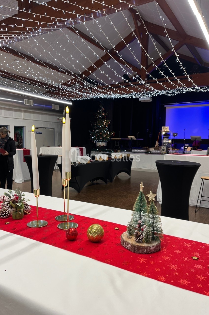 Salle décorée pour Noël avec guirlandes lumineuses, table rouge ornée de bougies et décorations festives au premier plan.