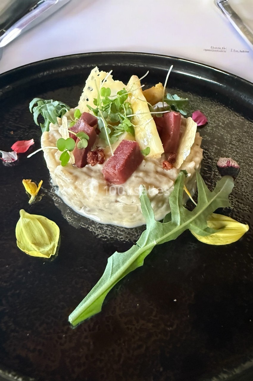 Assiette gastronomique avec risotto crémeux, morceaux de viande, asperges, roquette et pétales de fleurs comestibles.