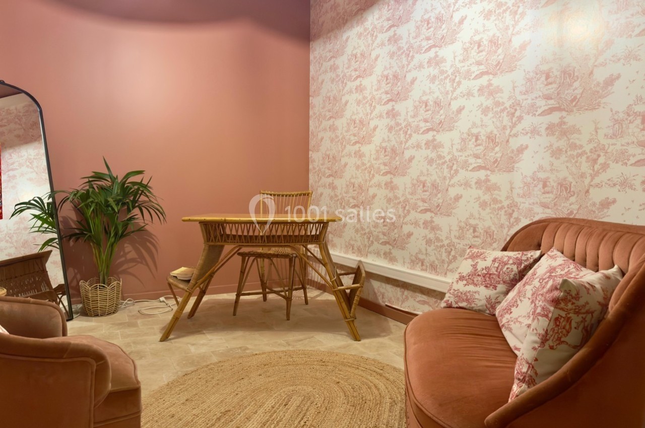 Salle décorée dans des tons roses avec un canapé, des fauteuils, une table en rotin et un mur à motifs floraux.