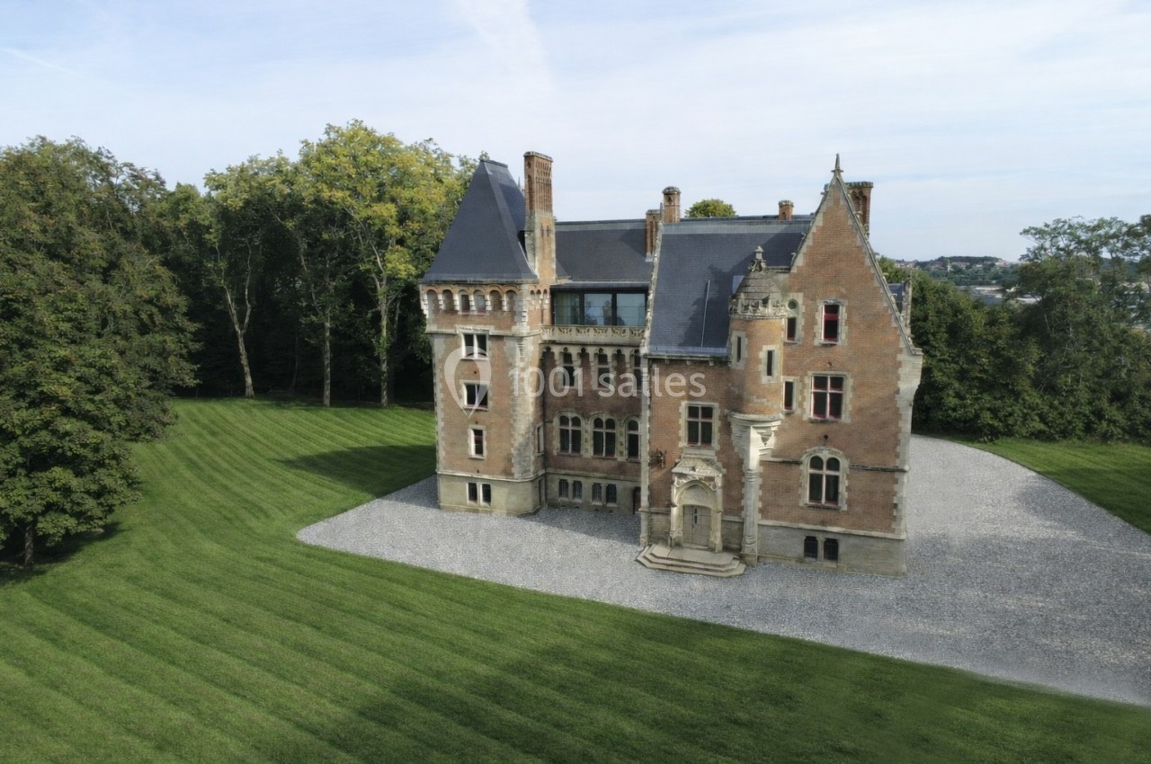 Vue aérienne d'un château en briques rouges entouré d'une pelouse bien entretenue et d'arbres.