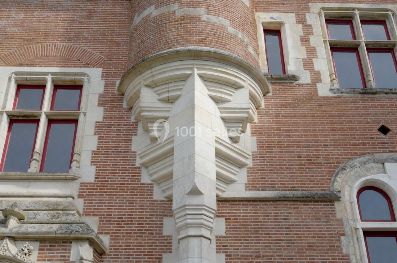 Détail architectural d'une façade en briques avec fenêtres à encadrements en pierre et une tourelle ornée.